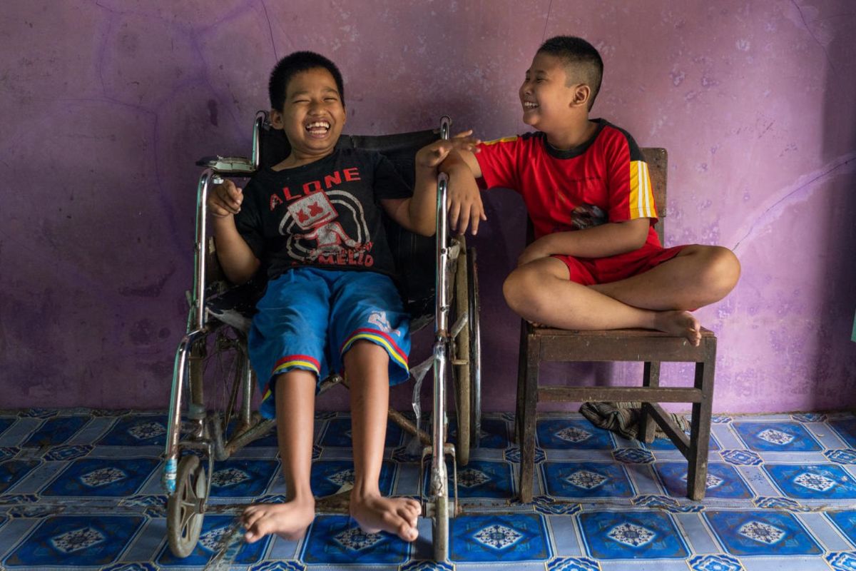 A boy in a wheelchair with his friend sitting in a chair next to him